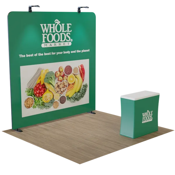 A trade show booth setup for Whole Foods Market, featuring a large banner with fruits, vegetables, and grains, standing next to a branded counter on a wooden floor. The banner text reads: 'Whole Foods Market. The best of the best for your body and the planet'.